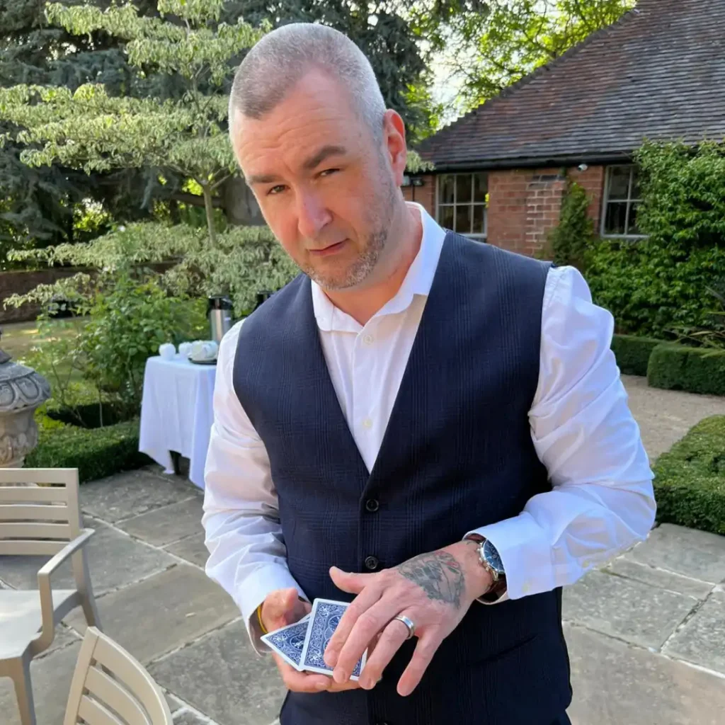 Main character of image is Tony Byrne, tony is wearing smart dress, holding playing cards. Tony is outside on a patio.